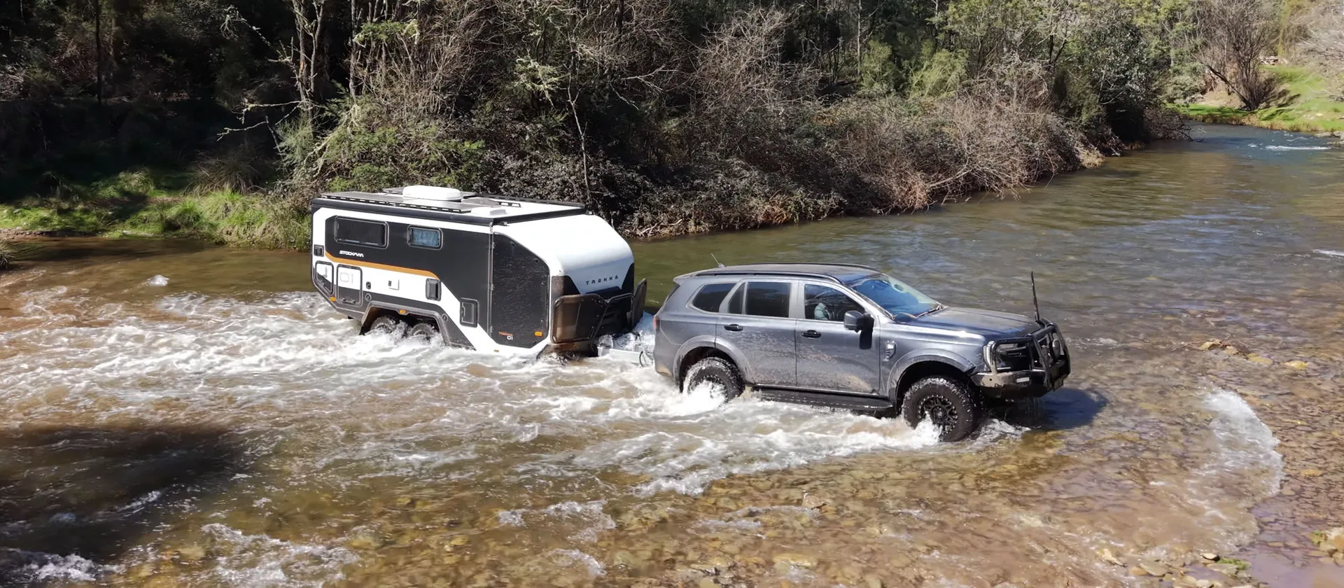A 4WD towing a Stockman Trekka through a shallow river